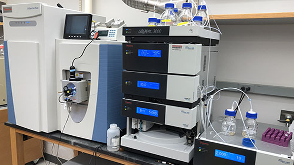 This image shows a sophisticated mass spectrometry system in a laboratory environment. The equipment appears to be a high-performance liquid chromatography (HPLC) system coupled with a mass spectrometer. 